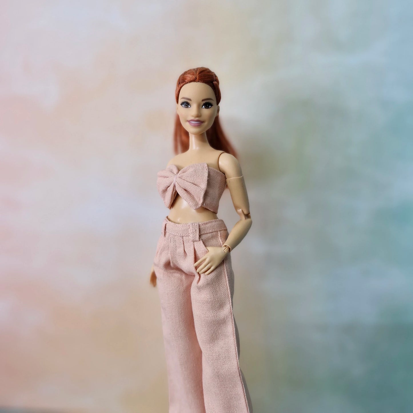 Close-up of Barbie Curvy doll wearing blush pink bow top and wide-leg pants.
