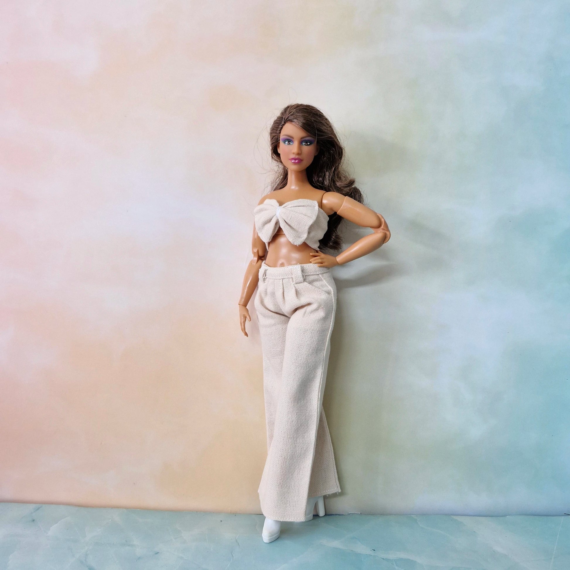 Full-body shot of Barbie Curvy doll in cream white bow crop top and wide-leg pants.
