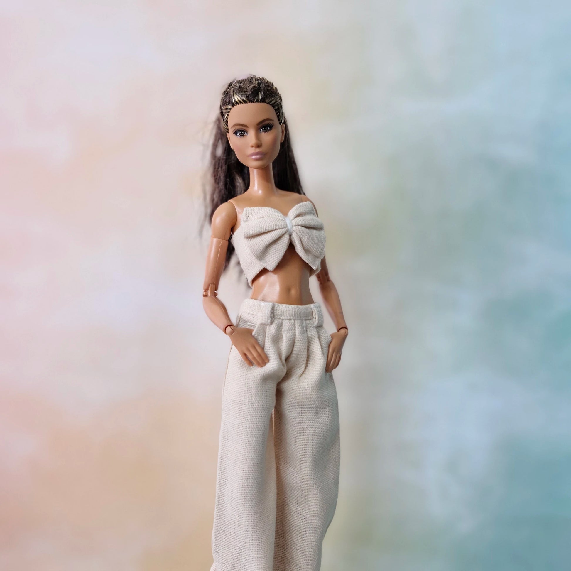Close-up of Barbie in cream bow top and wide-leg pants posing against pastel gradient.
