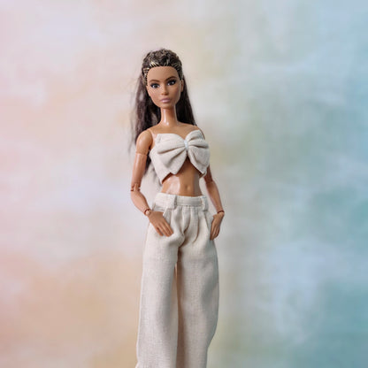 Close-up of Barbie in cream bow top and wide-leg pants posing against pastel gradient.
