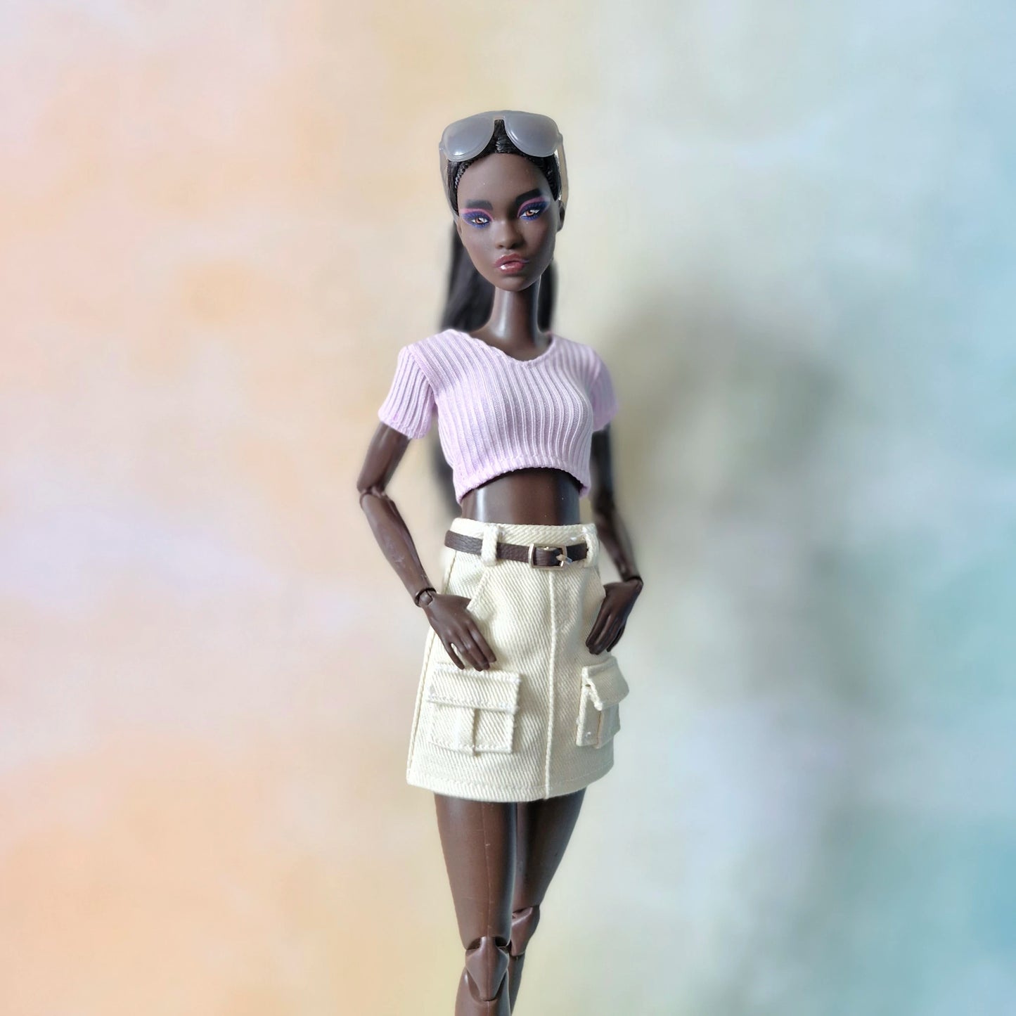 Black fashion doll wearing lilac ribbed crop top and cream white cargo mini skirt with pockets