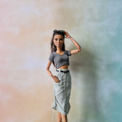 Barbie doll wearing a gray top and white skirt against a blurred background