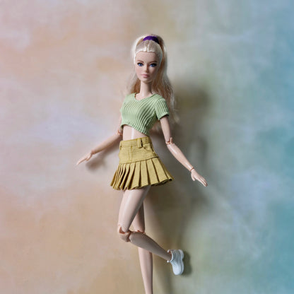 Blonde Barbie doll wearing pistachio green crop top and mustard yellow pleated tennis skirt