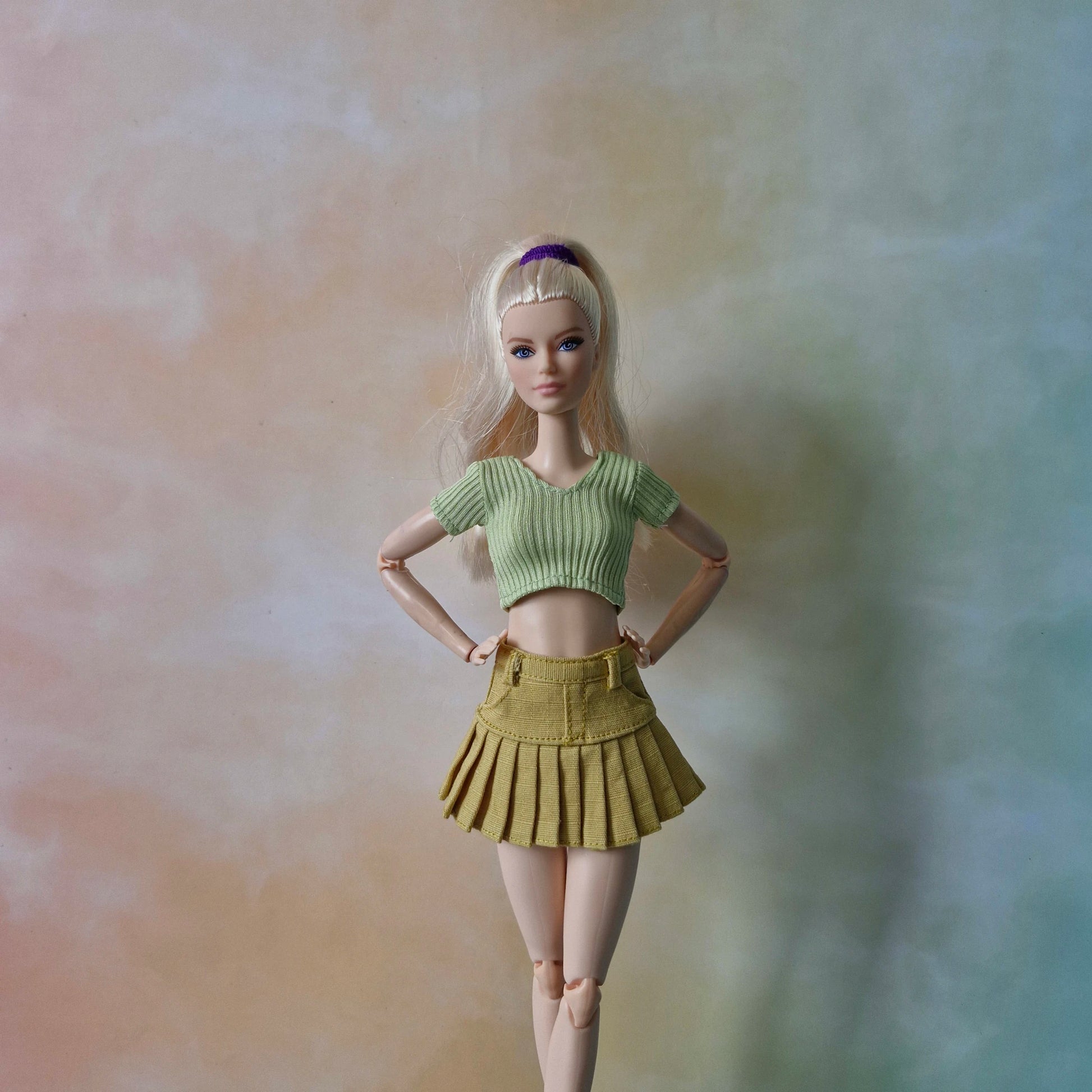 Barbie doll wearing a green top and yellow skirt against a gradient background