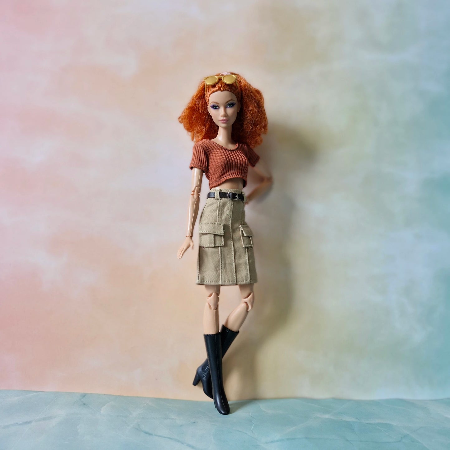 Barbie doll with red hair wearing a brown top and beige skirt against a gradient background