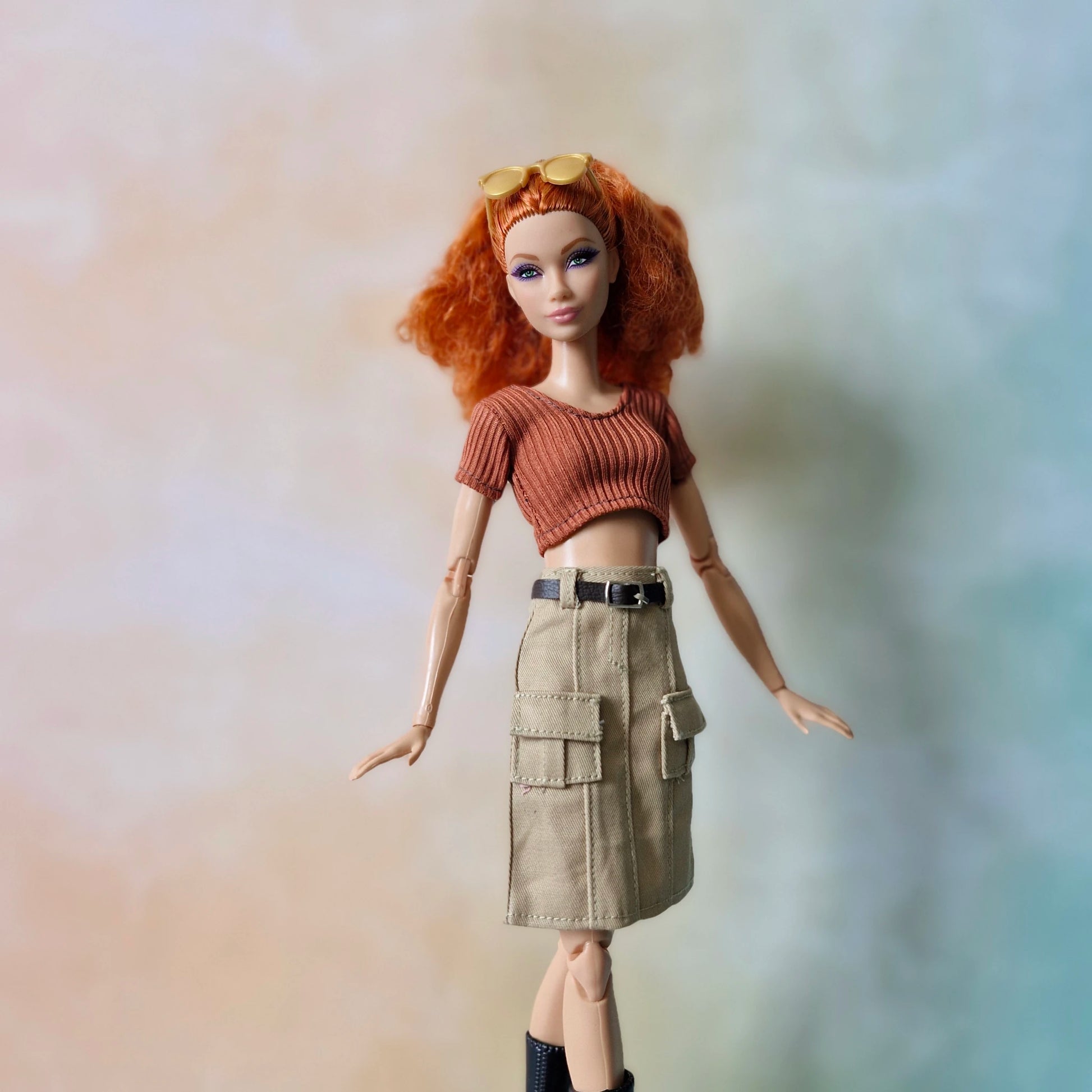 Doll with red hair wearing a brown top and beige skirt against a blurred background