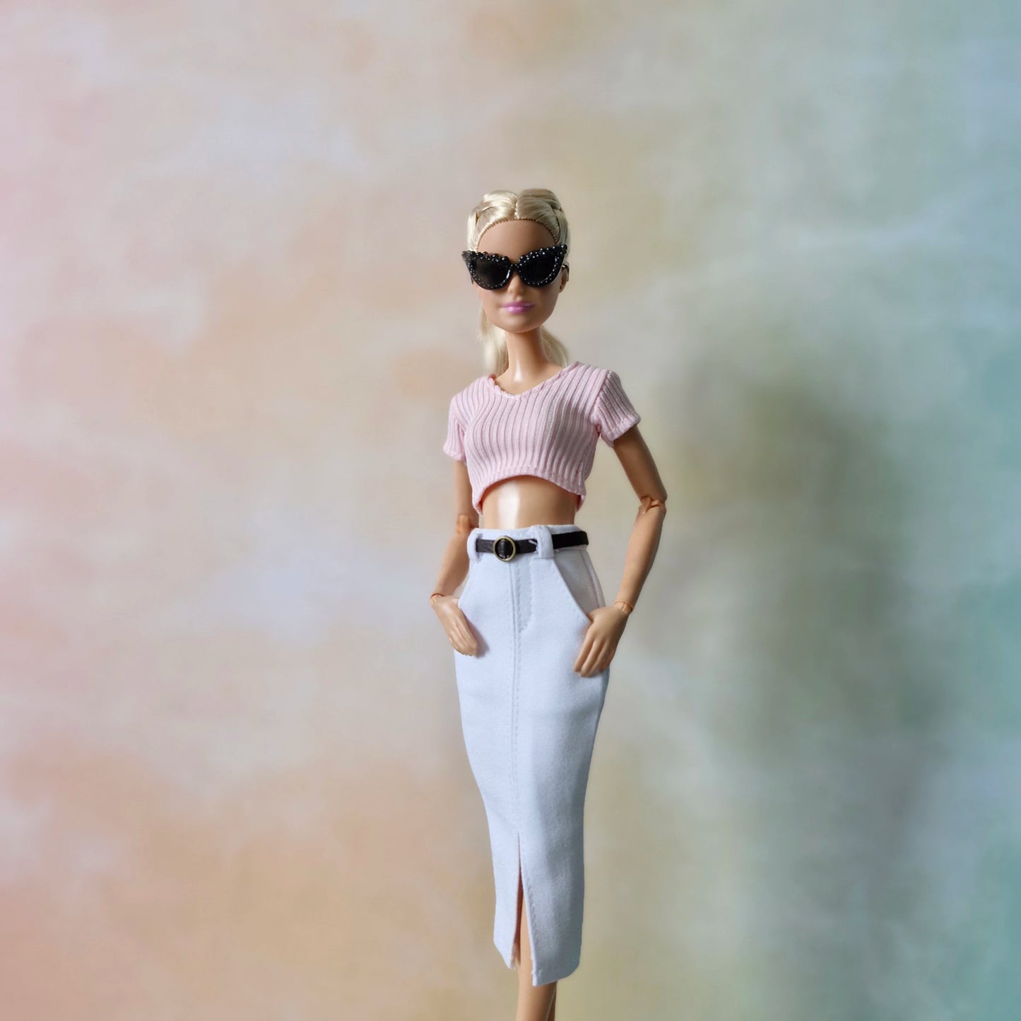 Barbie doll wearing a pink top and white skirt with sunglasses against a blurred background