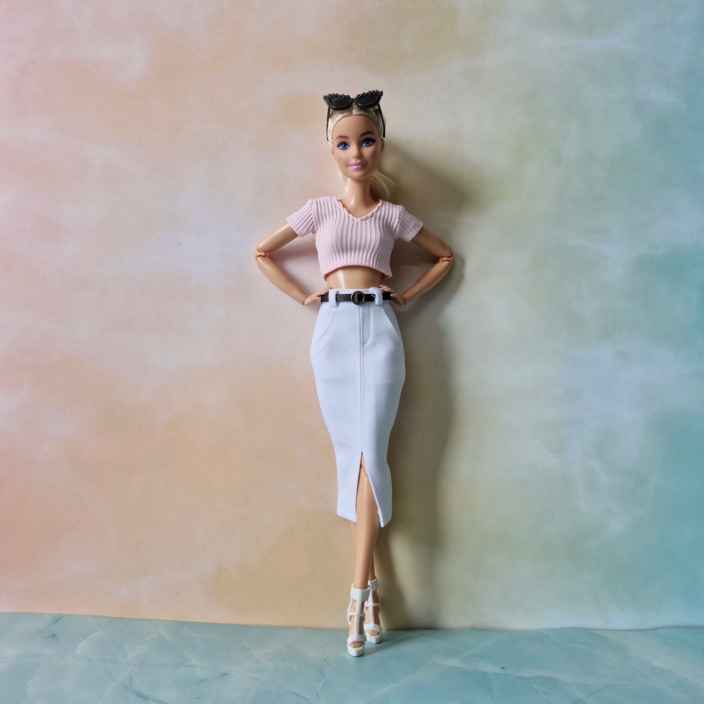 Barbie doll wearing a pink top and white skirt against a gradient background