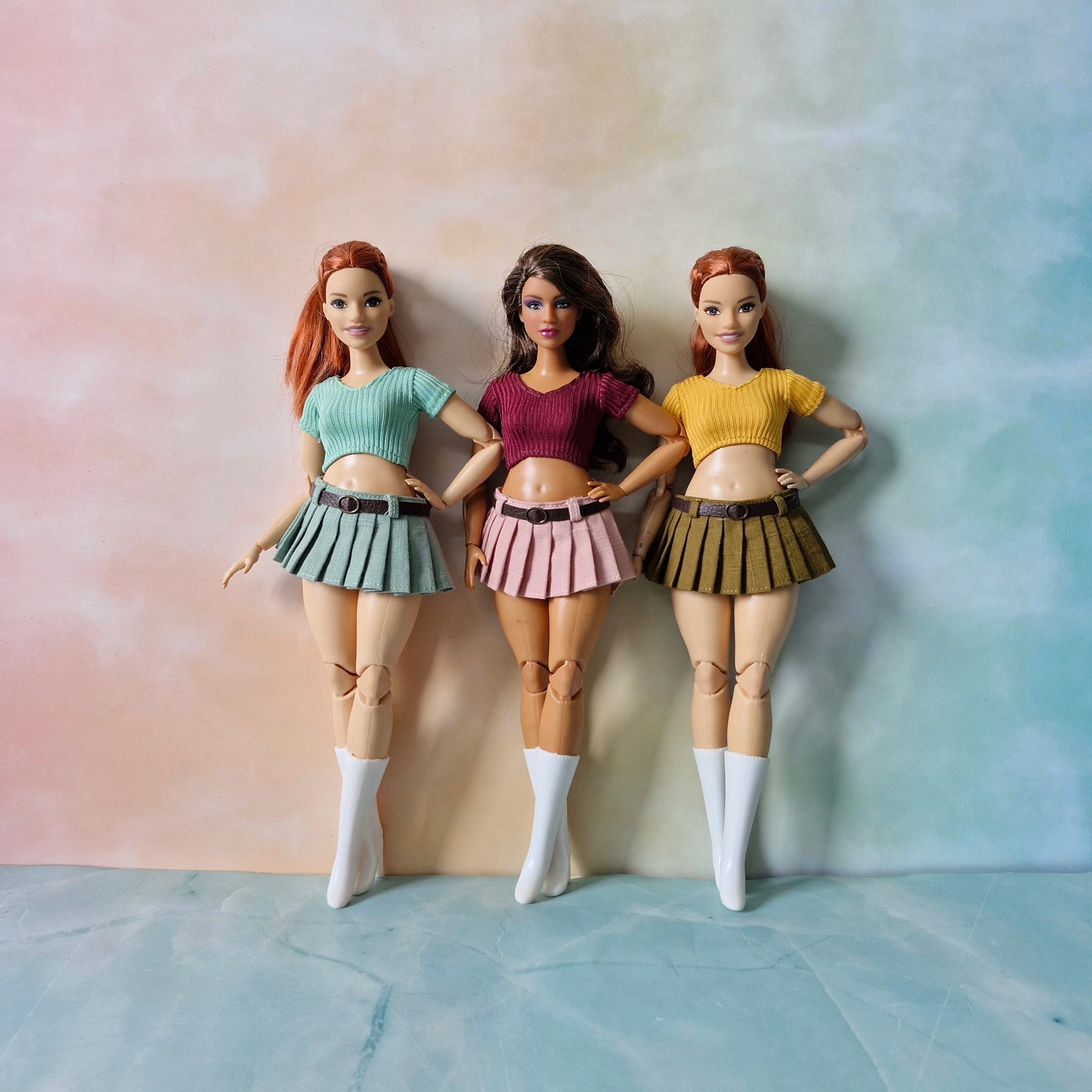 Three curvy fashion dolls modeling pleated mini skirts and crop tops in green pink and yellow