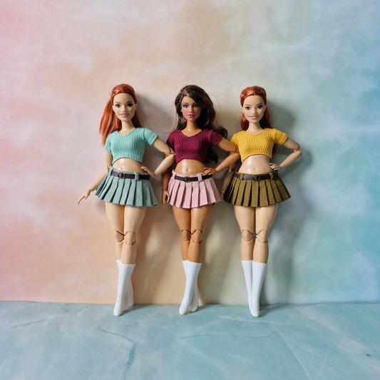 Three curvy fashion dolls modeling pleated mini skirts and crop tops in green pink and yellow