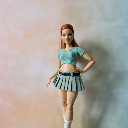 Curvy doll wearing sage green ribbed crop top and matching pleated skirt with belt