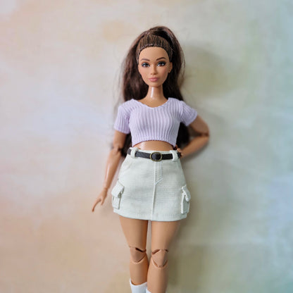 Barbie doll wearing a white crop top and beige skirt against a plain background