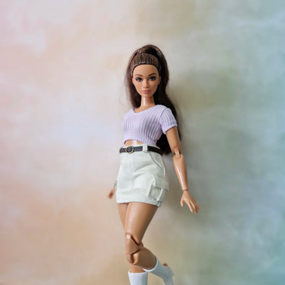 Barbie doll wearing a purple top and beige skirt against a gradient background