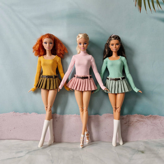 Three Barbie dolls modeling mix and match long sleeve tops and pleated skirts in yellow pink and green