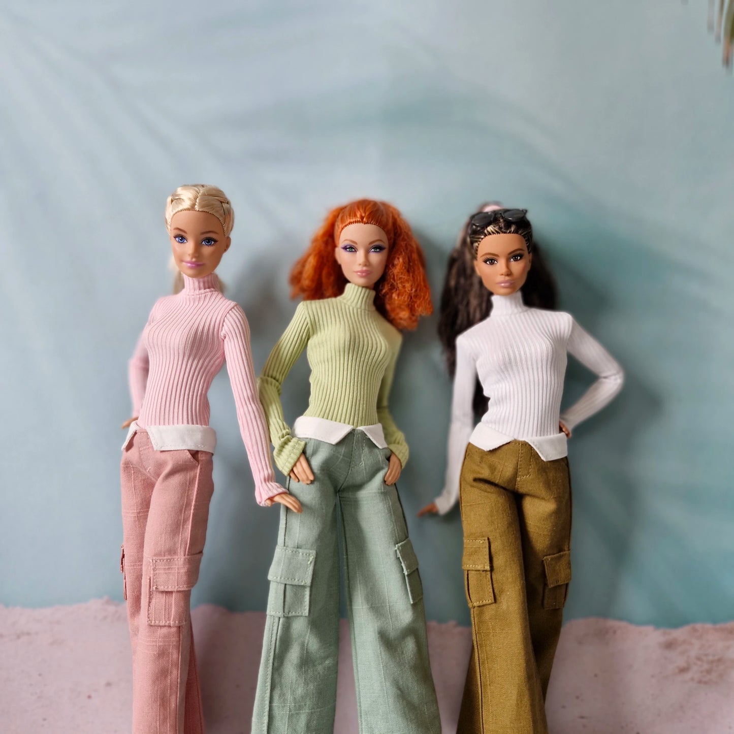 Three Barbie dolls wearing turtleneck tops and cargo pants in pink green and brown