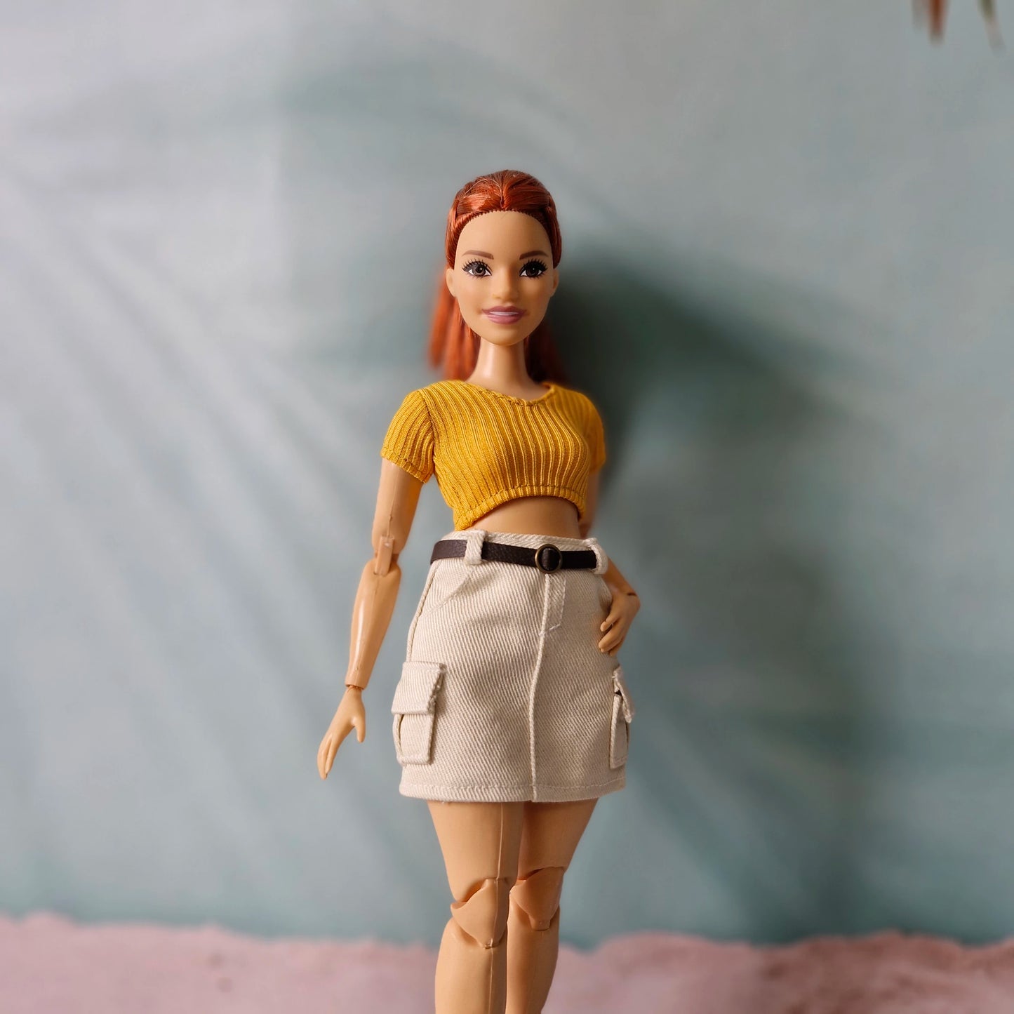 Close up of made to move curvy doll wearing mustard yellow knit top and cream skirt