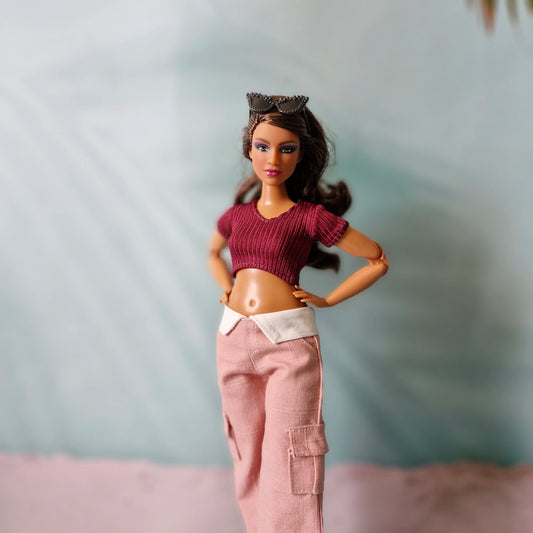 Curvy brunette fashion doll posing in burgundy ribbed crop top and pink cargo trousers