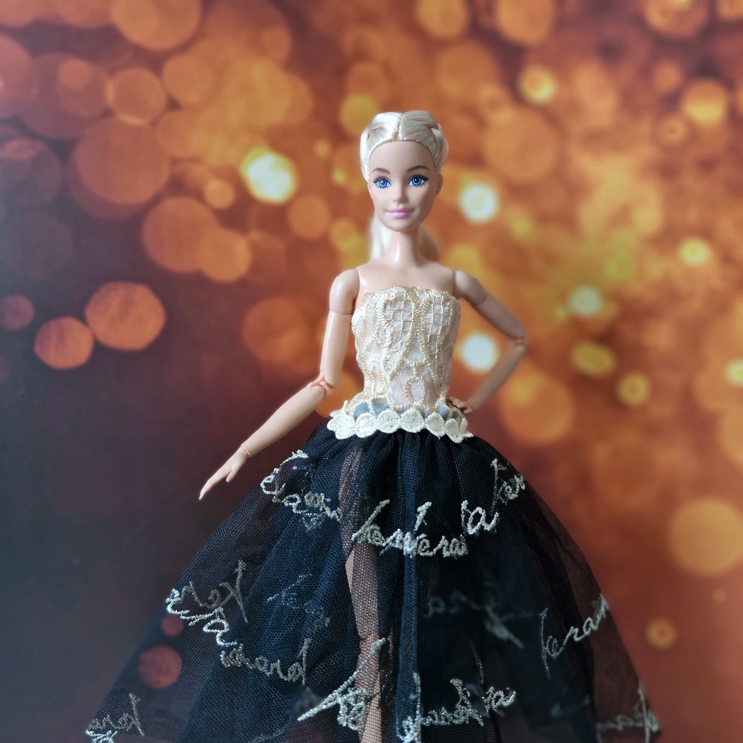 Blonde Barbie doll wearing an elegant gold lace bodice and black tulle dress with gold text embroidery