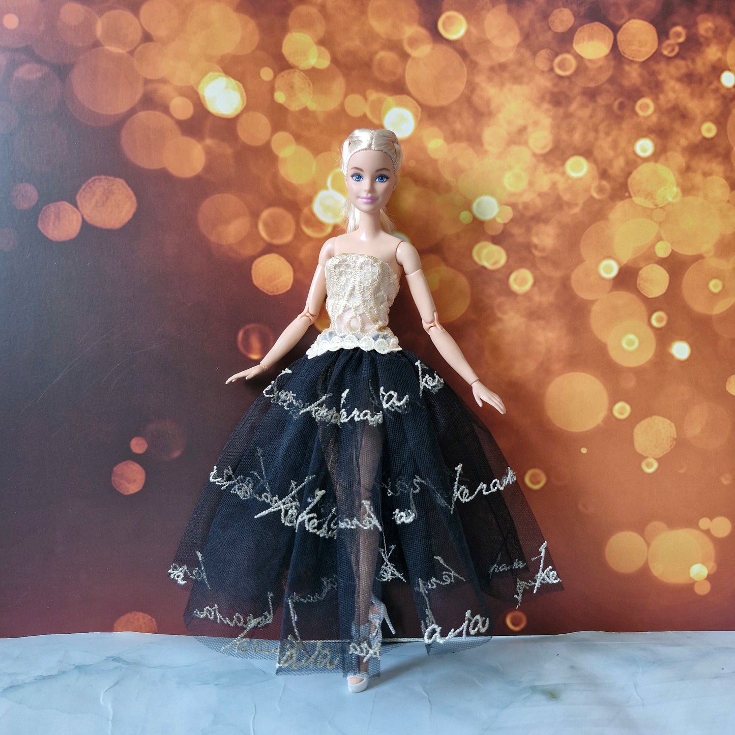 Full body view of Barbie doll in a high-low black tulle skirt and gold lace top evening gown