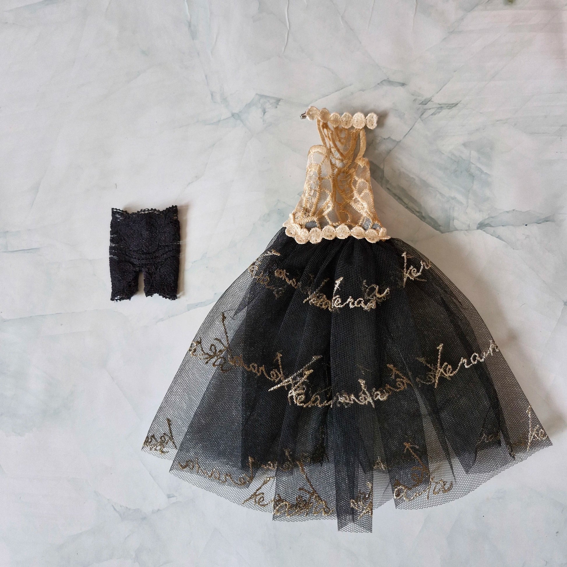 Flat lay of Barbie doll clothes showing a gold lace and black tulle dress next to black lace shorts