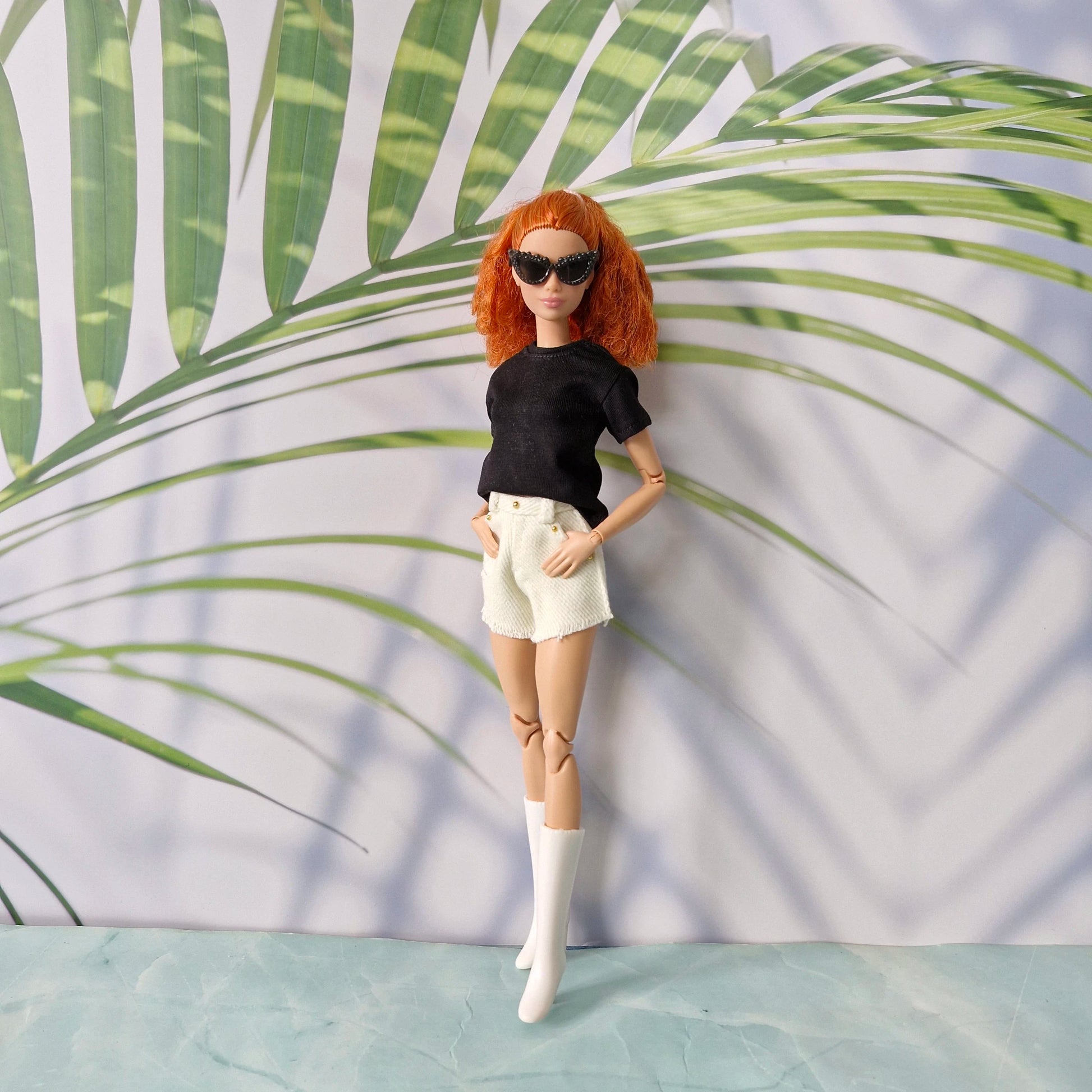 Redhead Barbie doll standing with hands in pockets wearing black t-shirt, white shorts, and boots