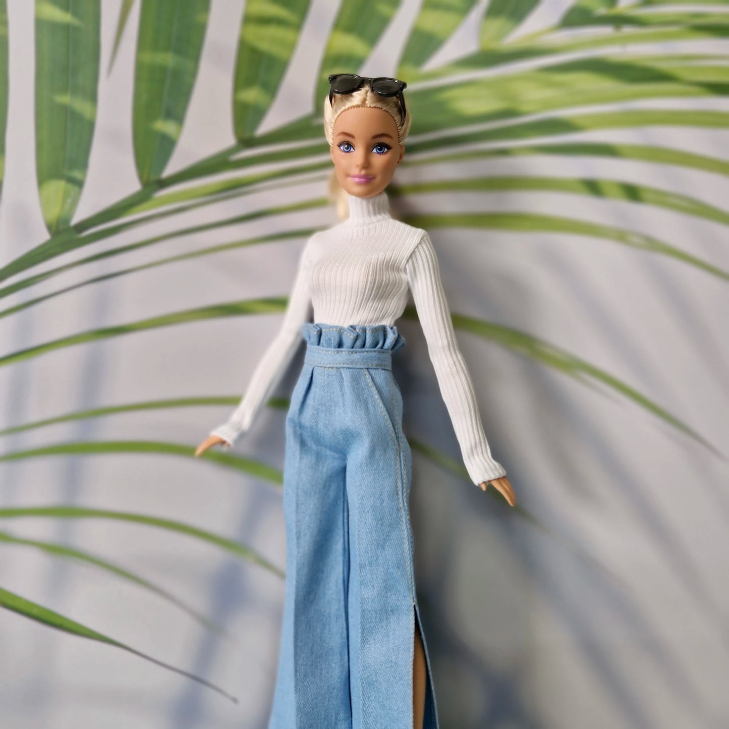 Barbie doll in a white sweater and blue pants standing against a leafy background