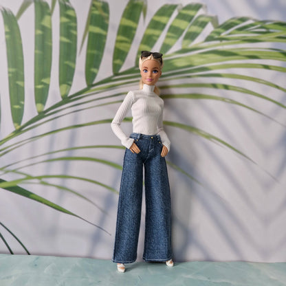 Blonde Barbie doll wearing a white ribbed turtleneck and dark blue wide leg jeans standing against a tropical background