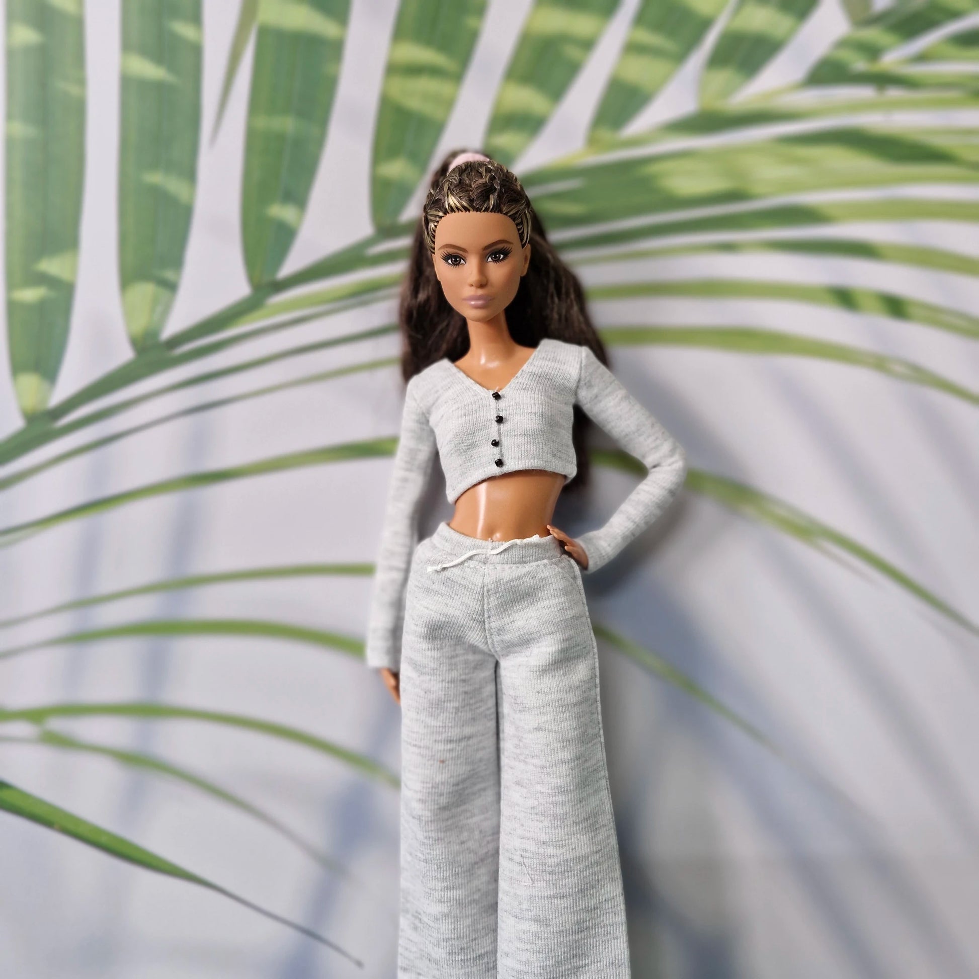 Barbie doll in a gray outfit standing against a leafy green background