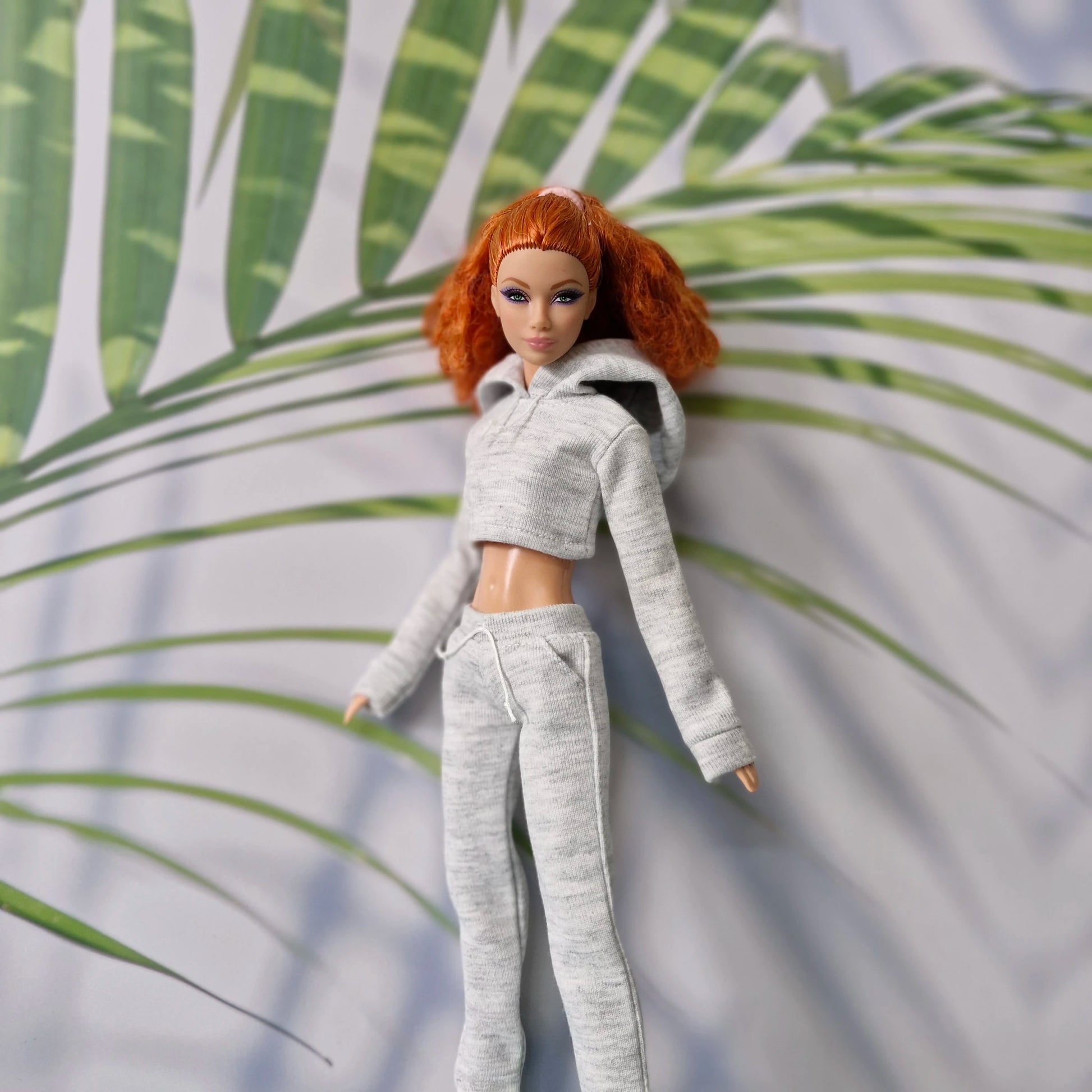 Redhead Barbie doll laying down in a grey cropped hoodie and joggers