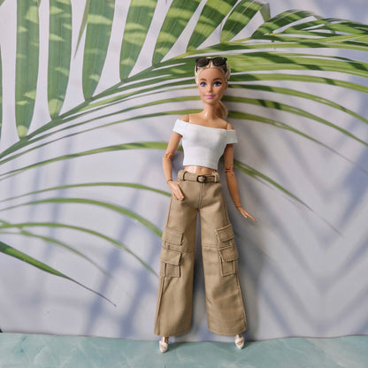Barbie doll wearing a white top and beige cargo pants against a leafy background