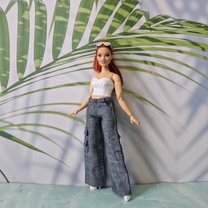 Barbie doll wearing a white top and gray cargo pants against a leafy green background