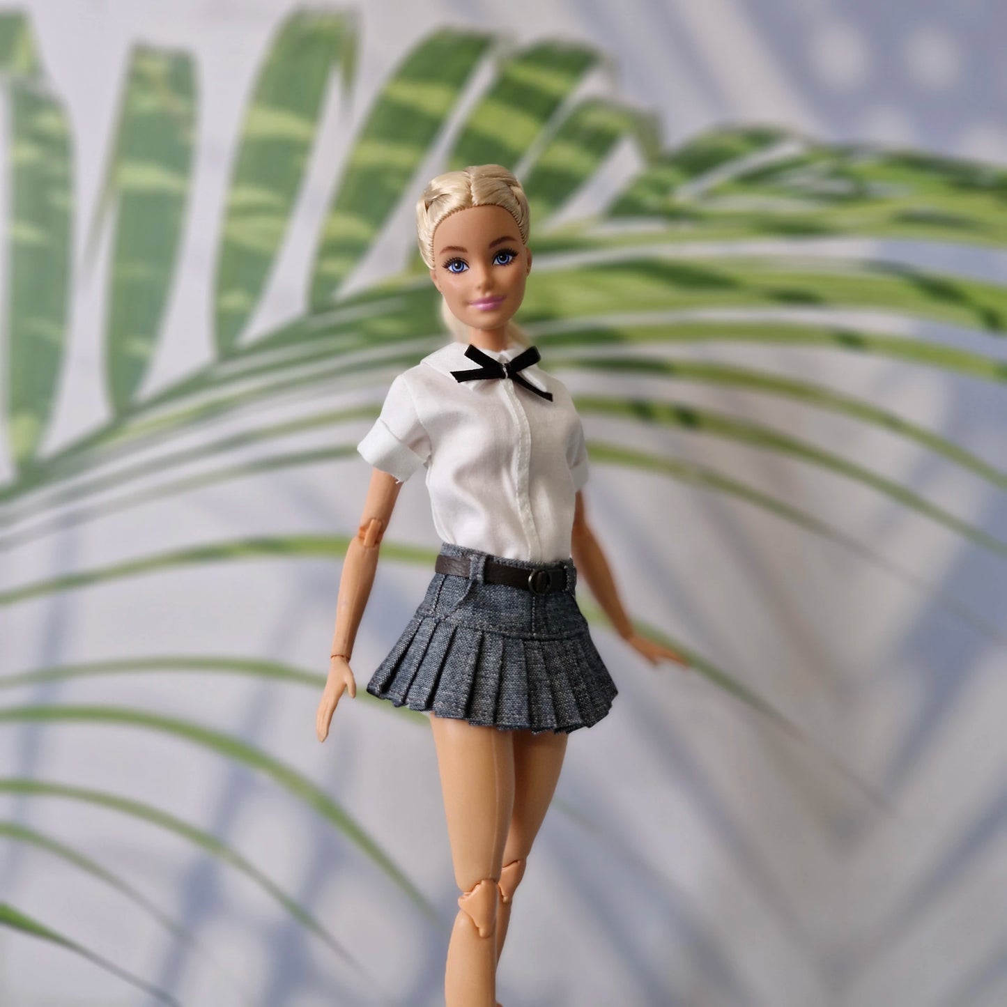 Close up of blonde Barbie doll wearing a schoolgirl style white shirt and denim pleated mini skirt
