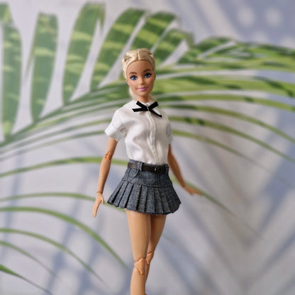 Close up of blonde Barbie doll wearing a schoolgirl style white shirt and denim pleated mini skirt