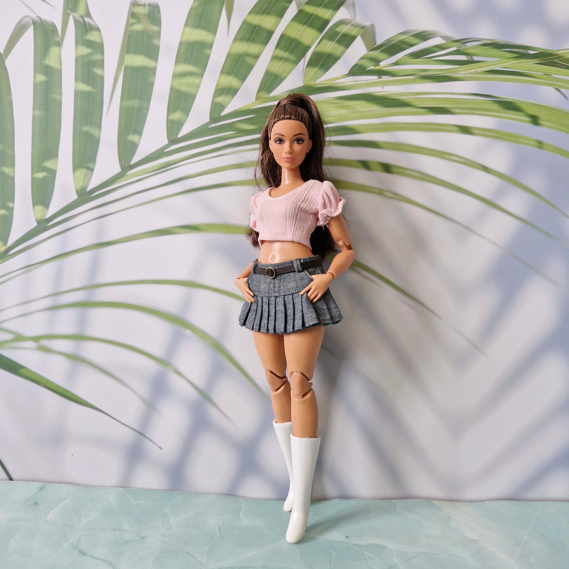 Curvy Barbie doll wearing a pink puff sleeve crop top and denim pleated skirt with tall white boots