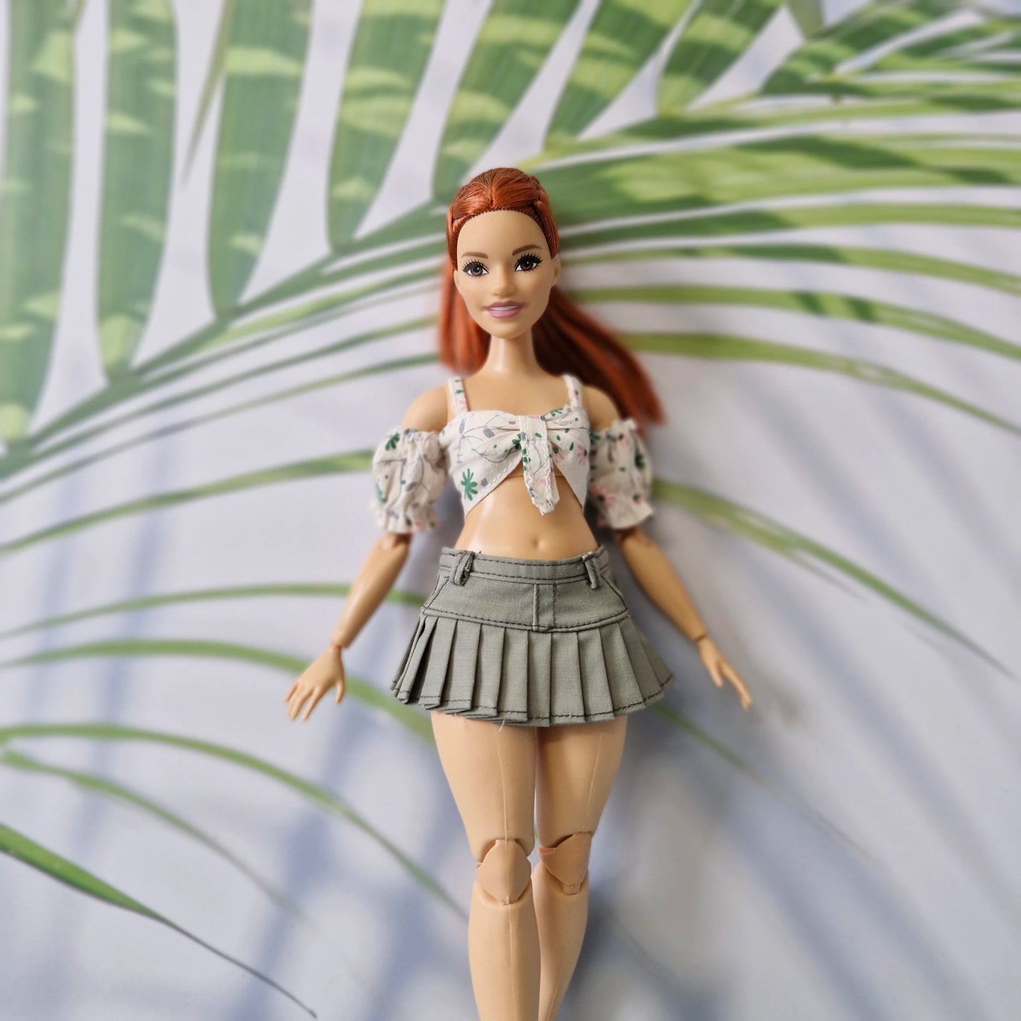 Barbie doll with red hair and a floral top and skirt against a leafy green background