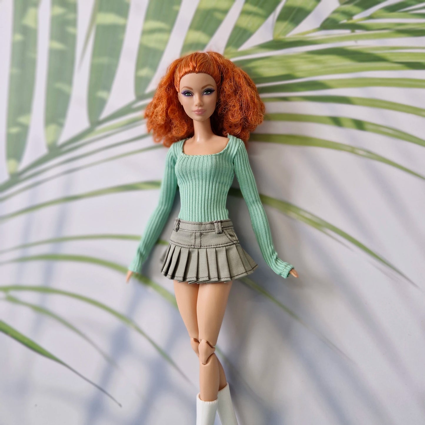 Standard redhead Barbie doll lying down wearing a green long sleeve ribbed top and olive pleated skirt