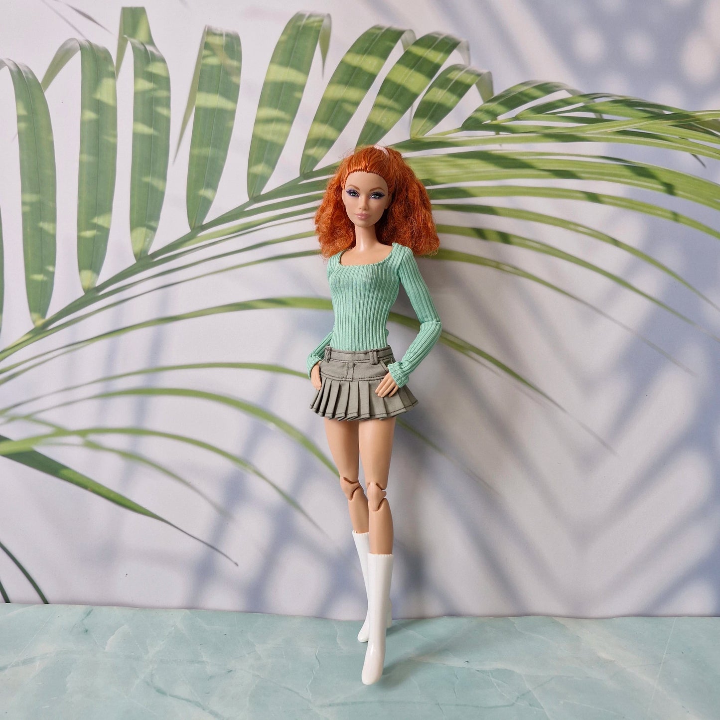 Barbie doll with red hair and green outfit standing against a leafy background