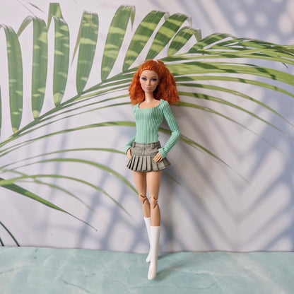 Barbie doll with red hair and green outfit standing against a leafy background