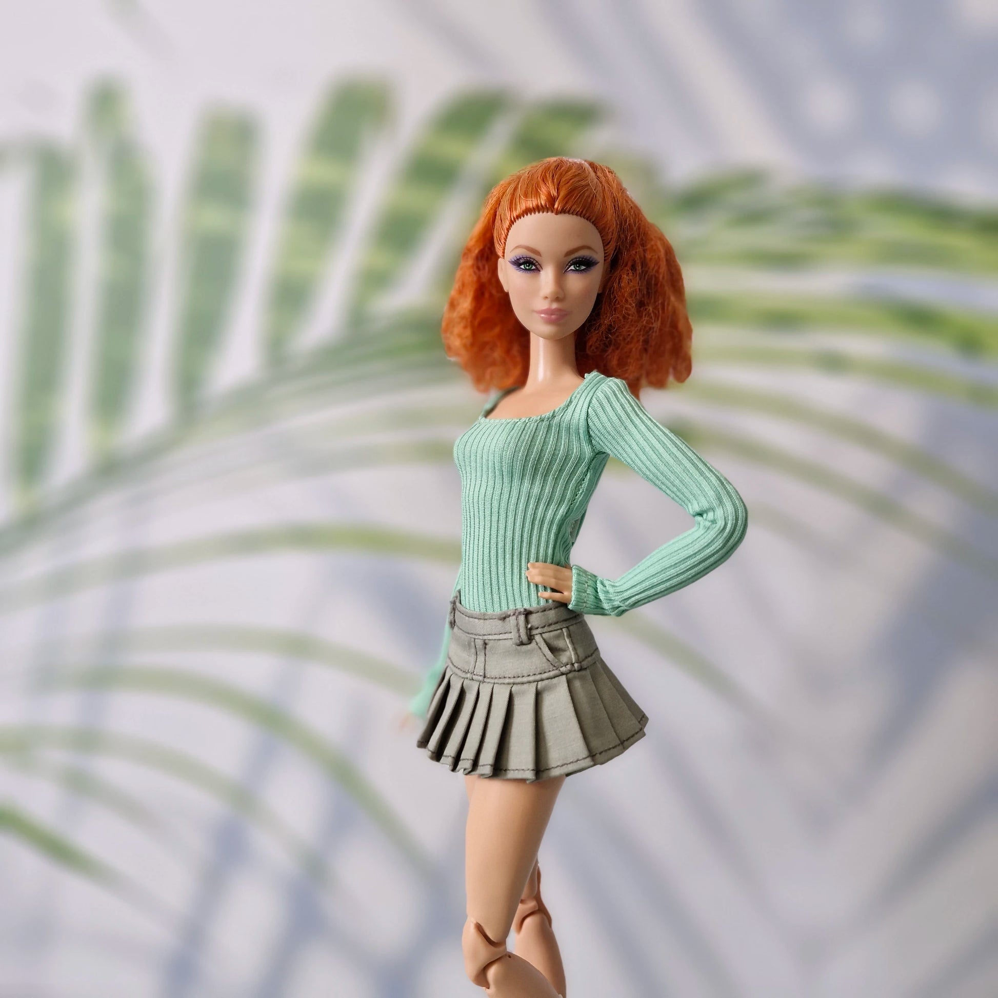 Barbie doll with red hair wearing a green sweater and skirt against a leafy background
