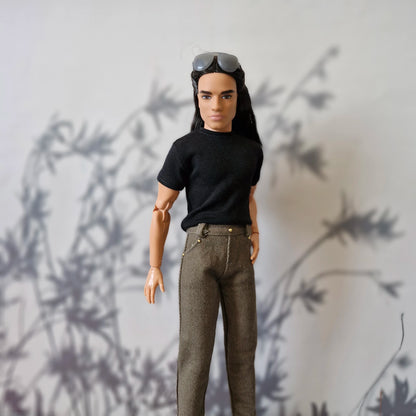 Close up of Ken doll in a black tee and brown pants with sunglasses on his head