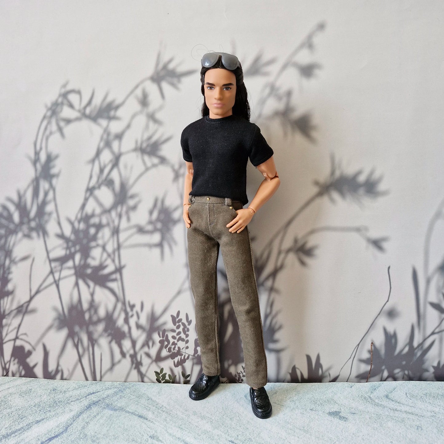 Full length view of Ken doll wearing a black t-shirt, brown pants, and black shoes