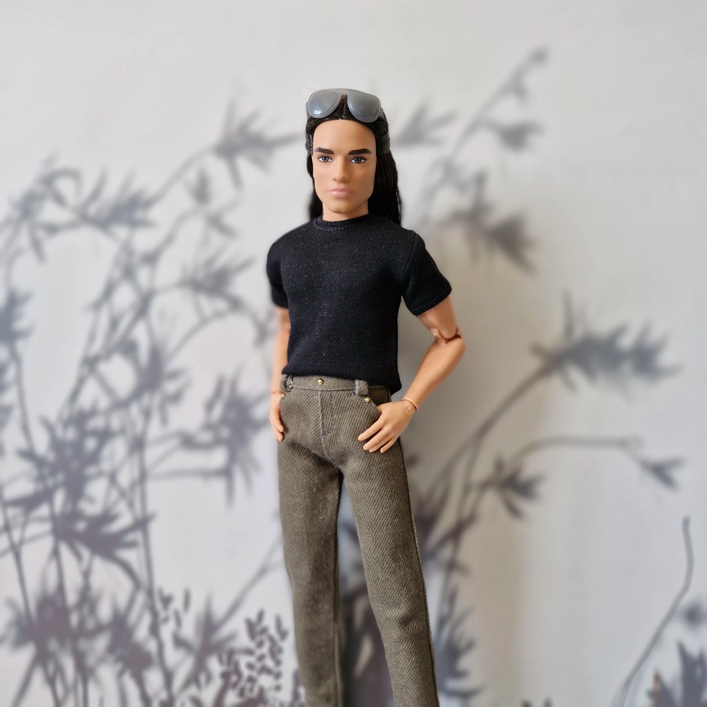 Ken doll standing with hands in pockets wearing a casual black shirt and brown pants