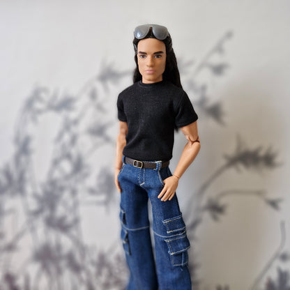 Ken doll standing with hands in pockets modeling a black tee and baggy blue cargo jeans