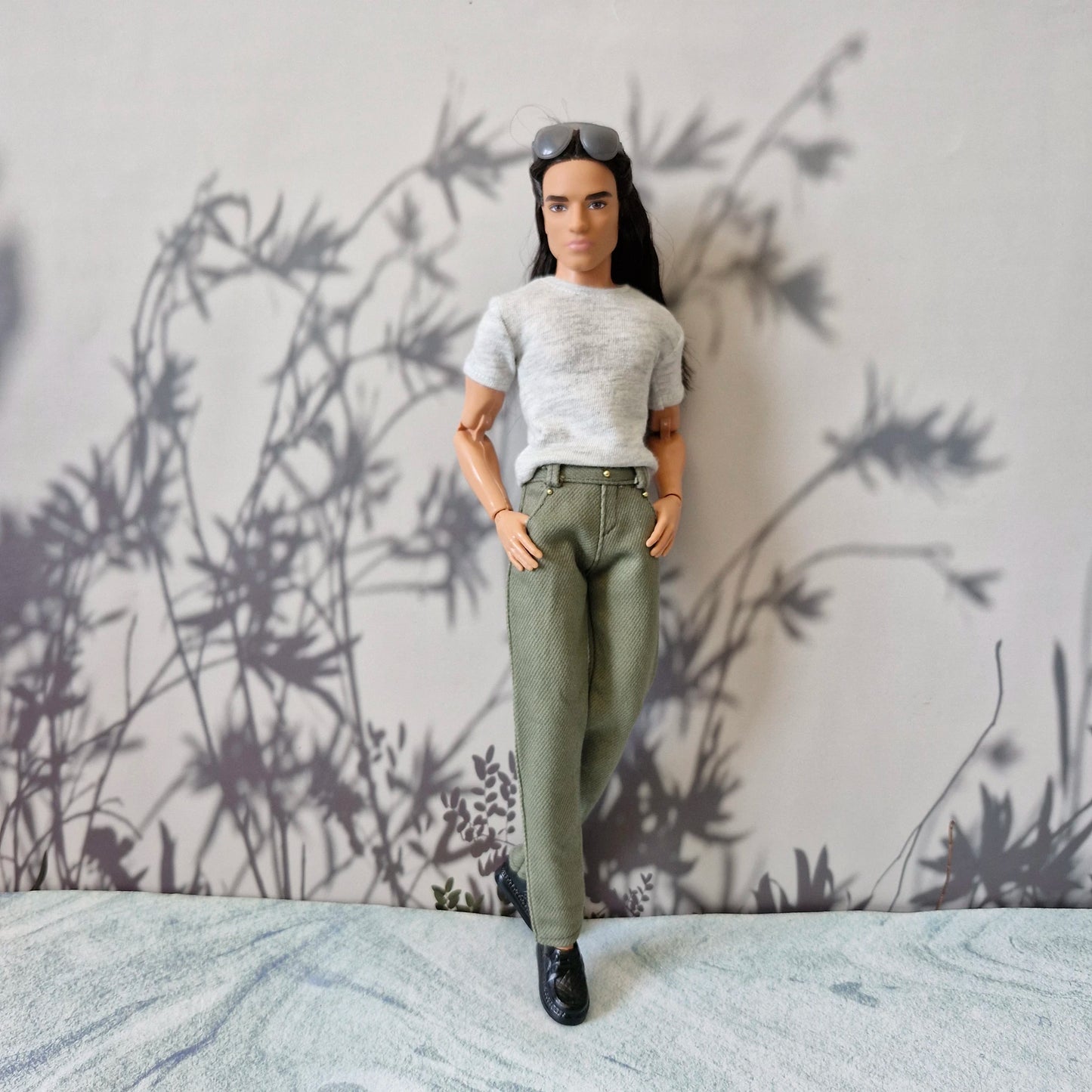 Ken doll posing casually with hands in pockets wearing a grey shirt and olive trousers