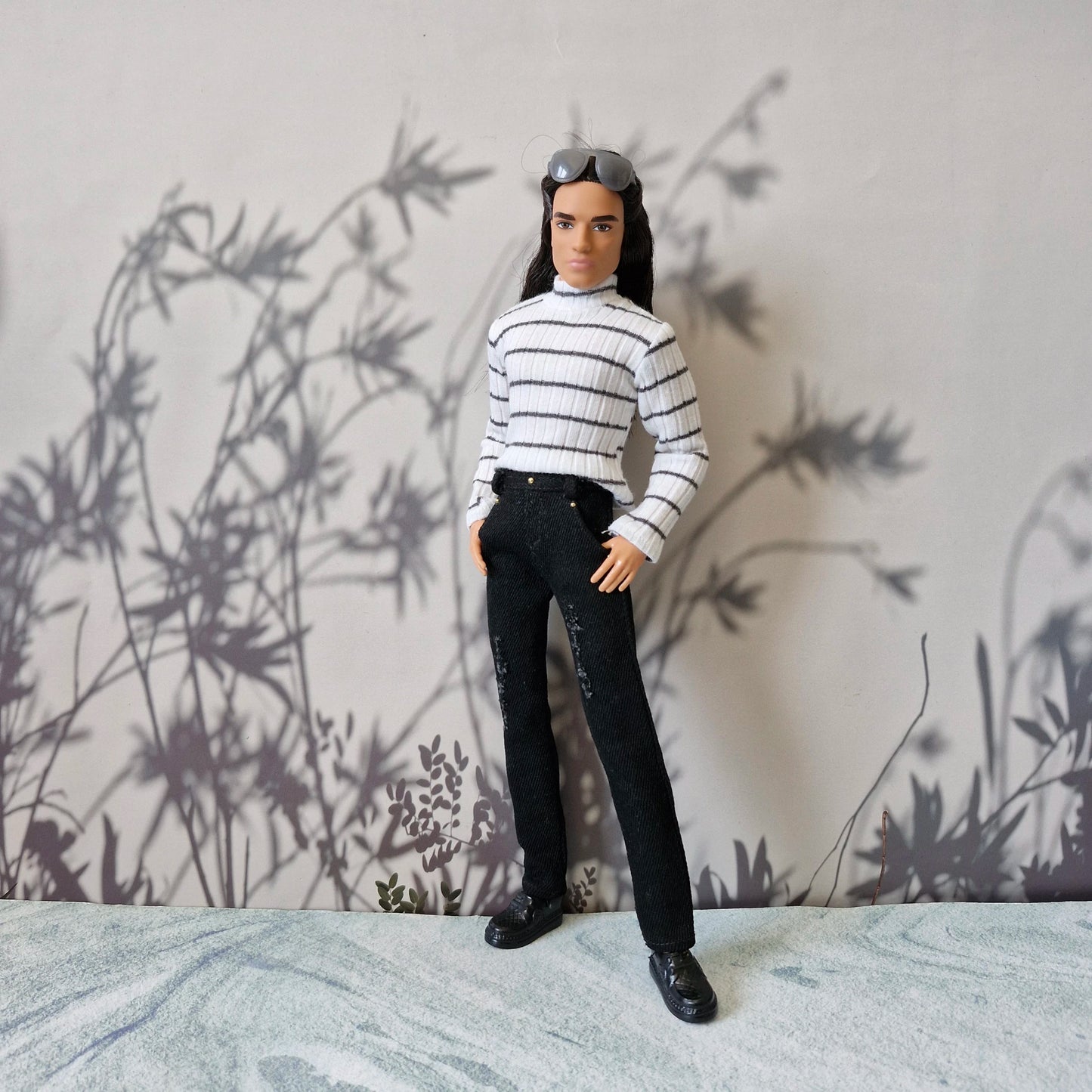 Ken doll posing with hands in pockets wearing a striped turtleneck and black distressed denim