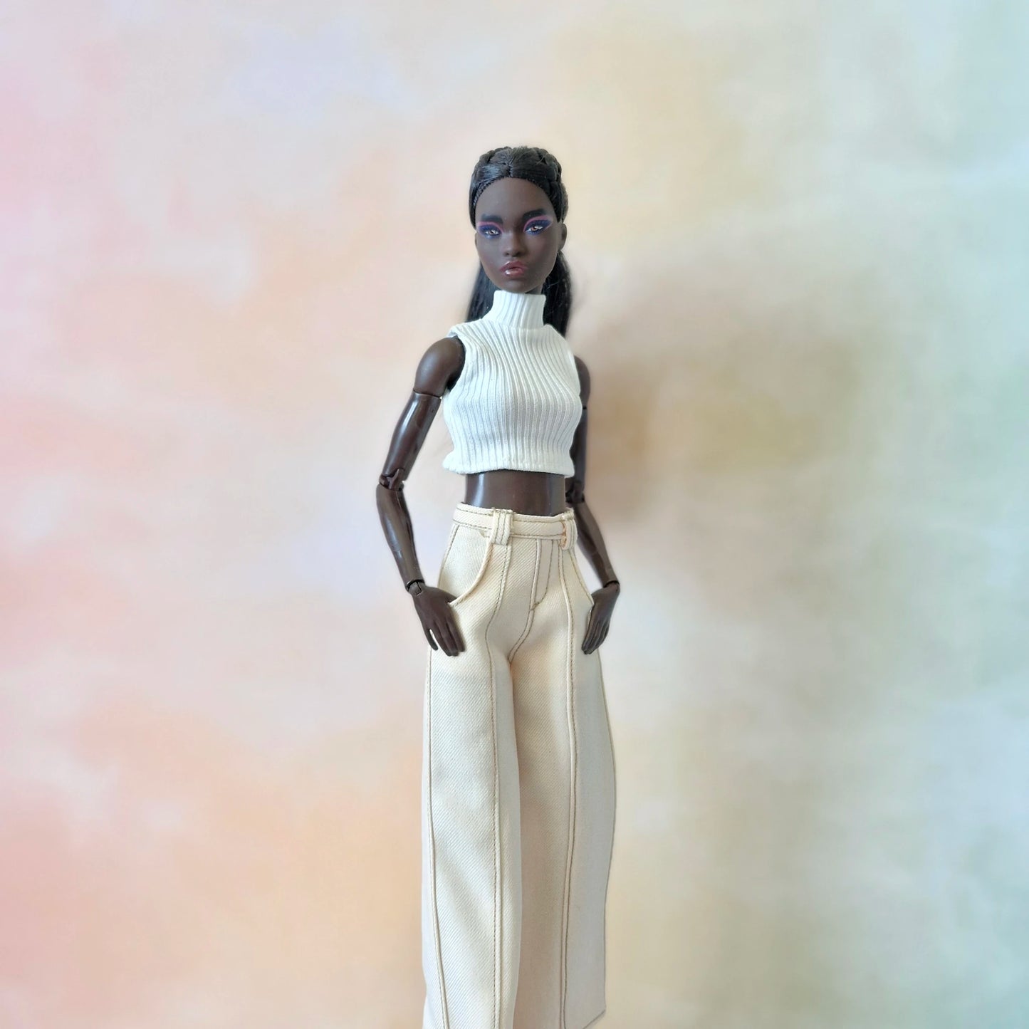 Doll wearing a white turtleneck and beige pants against a gradient background