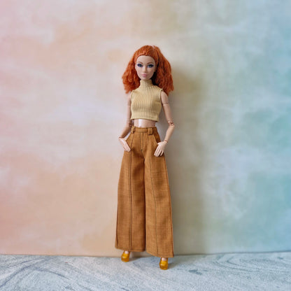 Doll wearing a beige top and brown pants against a gradient background