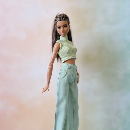 Barbie doll wearing a green sleeveless top and light blue pants against a gradient background