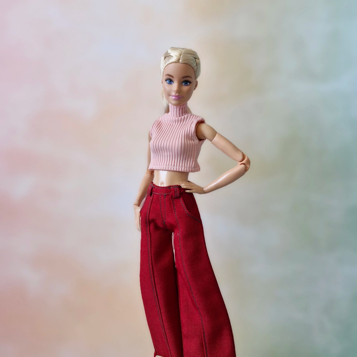 Barbie doll wearing a pink top and red pants against a blurred background