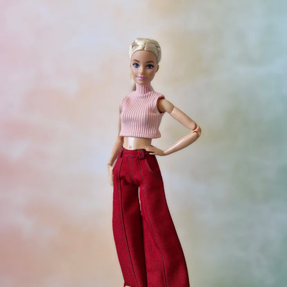 Barbie doll wearing a pink top and red pants against a blurred background